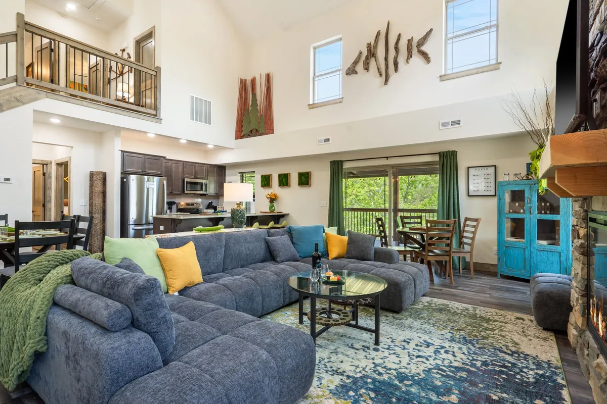 A spacious, sunlit interior featuring a large sectional sofa positioned near a stylish dining area, with artistic wall decor and expansive windows providing views and natural light. The space is designed to host family gatherings, with areas for relaxing, entertaining, and enjoying meals together.