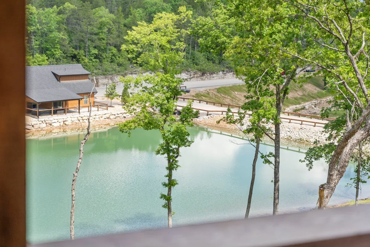 A peaceful fishing pond bordered by trees, with a cozy cabin in the background. The tranquil water reflects the sunset, inviting moments of relaxation, fishing, and connecting with nature.
