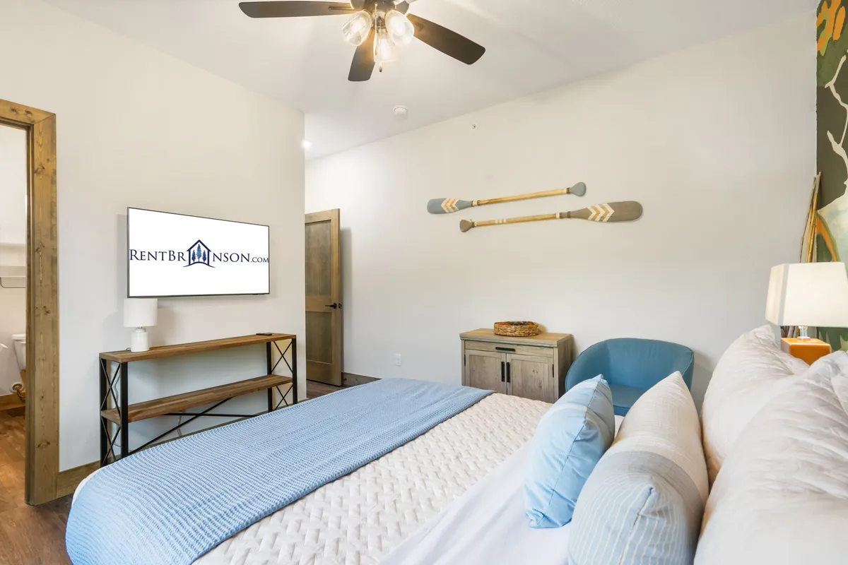 A cozy king-sized bed with decorative paddles on the wall, a nightstand with a lamp, and a television positioned for easy viewing. The room exudes warmth and comfort, with soft bedding and a layout ideal for relaxation or unwinding with a movie or book.