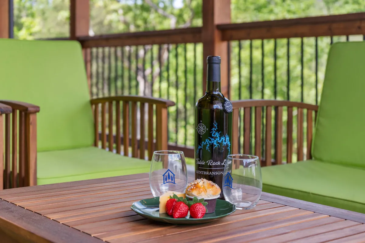 A cozy outdoor table set with a wine bottle, glasses, dessert plate, and green chairs, all positioned to take in sunset views. The scene suggests relaxation, alfresco dining, and memorable moments shared outdoors.