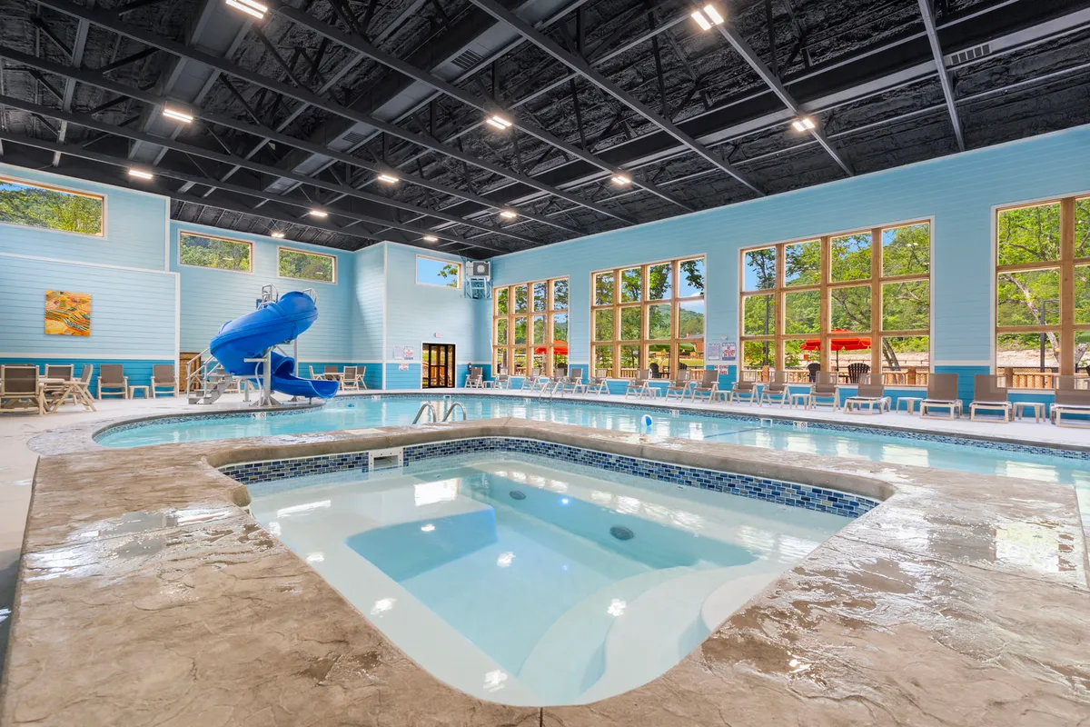 Inside, a bright indoor pool area features a swimming pool, water slide, jacuzzi, and lounge chairs. Sunlight streams through large windows, and the space is designed for joyful swimming, relaxing soaks, and group fun, offering both play and relaxation for guests.