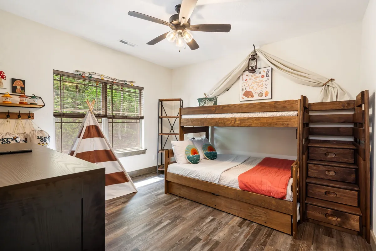A playful children's bunk room with a bunk bed (twin over full), a cozy teepee for imaginative play, and whimsical decorative items on shelves. The room feels adventurous and inviting, perfect for kids or extra guests.