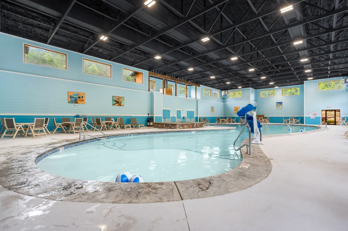 A bright, spacious indoor pool area with large windows flooding the space with natural light. Lounge chairs line the pool, and decorative artwork adds a cheerful touch. The scene captures both swimming and socializing activities, creating a leisurely, inviting environment.